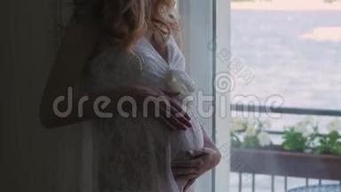 穿着白色连衣裙的孕妇正坐在窗边穿着白色蕾丝连衣裙.. 从上面看。 幸福的女人期待着